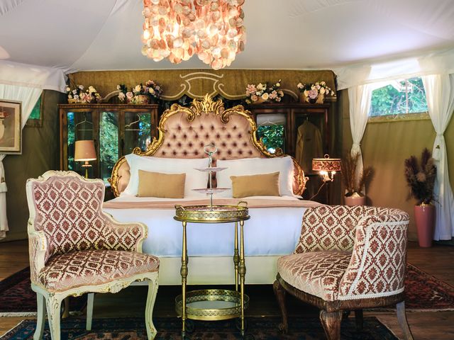 A luxury glamping tent with regal upholstered chairs and headboard under an intricate chandelier.