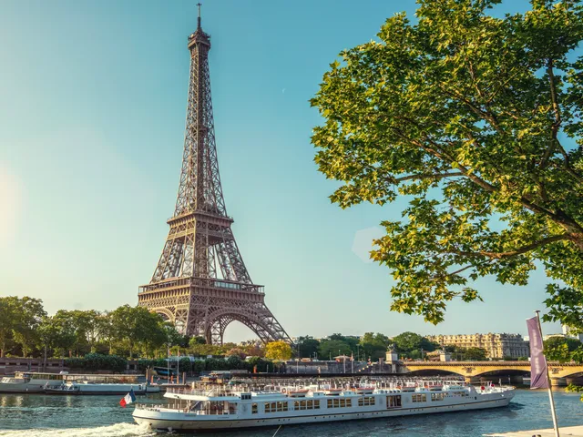 A view of the Eiffel Tower with a passing boat in the river.