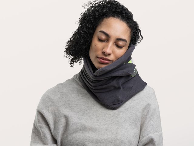 A woman sleeps with her head positioned against a scarf-style neck pillow.