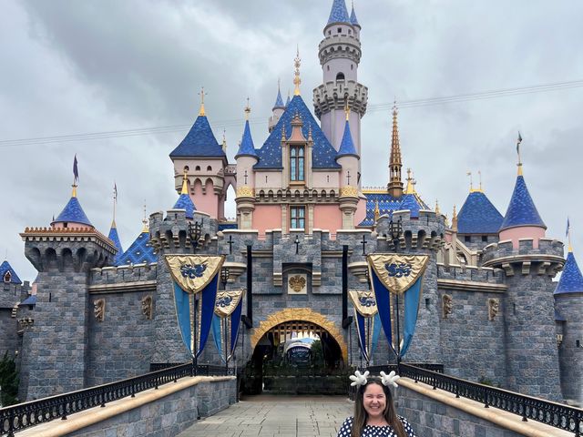 A woman wearing Disney ears poses in front of the castle at Disneyland.