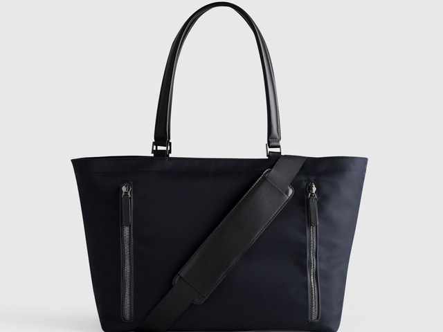 A large black tote bag with top handles and a crossbody strap, against a white background.