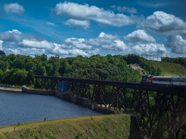 The Agawa Canyon train crossing a bridge over a river in Canada surrounded by green trees.