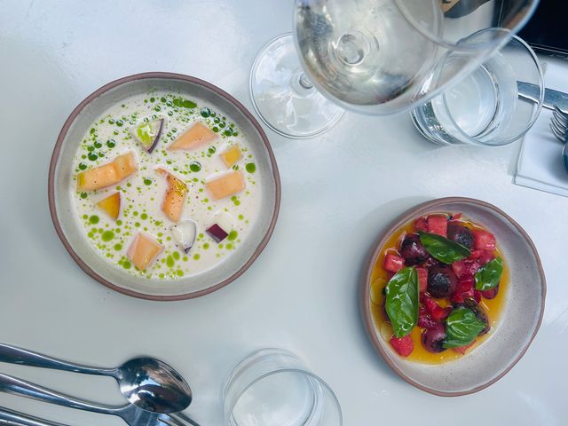 An overhead shot of a table with a white tablecloth and two gourmet dishes of food.