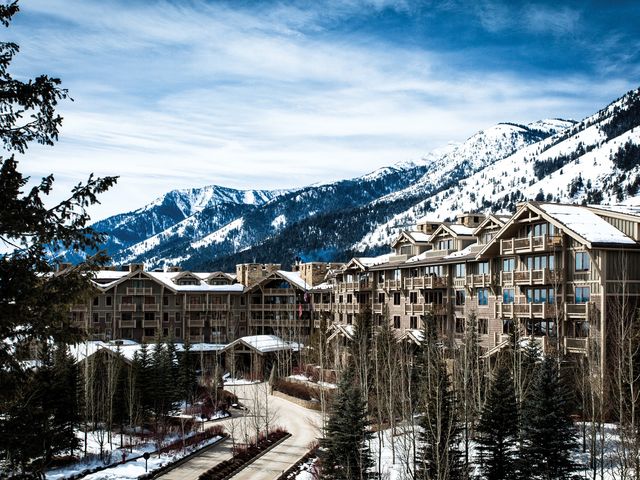The exterior of Four Seasons Resort and Residences Jackson Hole, featuring stately lodge-like architecture set against snow-capped mountains and ski runs.