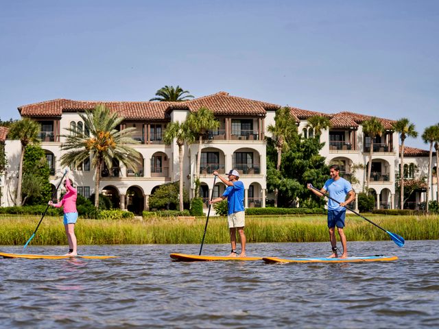 Three people paddleboard on the water in Georgia next to The Cloister at Sea Island hotel. 