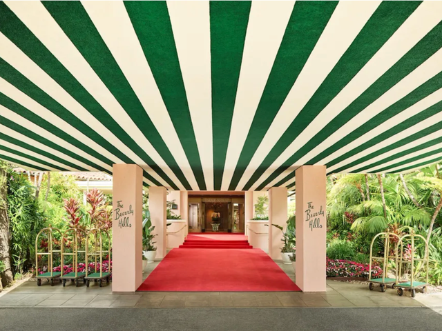 The iconic entrance to The Beverly Hills Hotel with it's green and white striped awning, pink columns, and lush landscaping.
