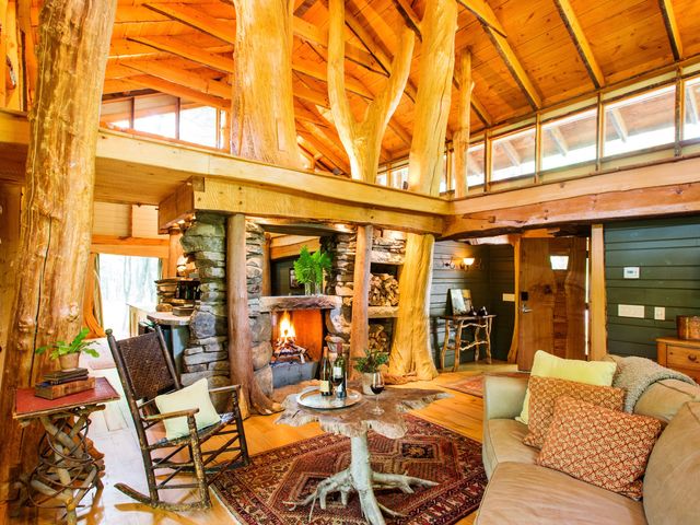 The Woodlands Cottage at Winvian with tree trunks, light wood accents, a stone fireplace, a couch, and cozy cabin vibes.