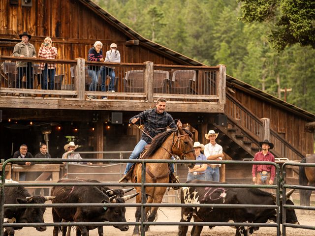 A man on a horse in a pen with cows and people watching.