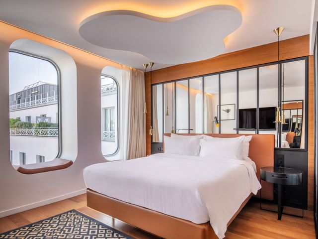 A hotel room with a bed in front or mirror panels, contemporary furniture, and windows at Renaissance Paris Republique Hotel.