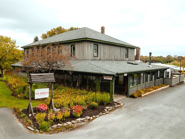 A farm house style building with flowers and bushes out front and trees with autumn foliage around it.