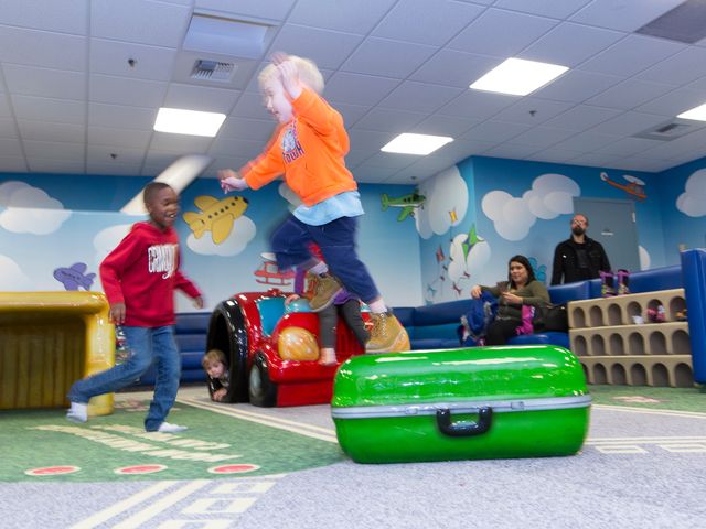 Two children who are slightly blurred out from action play in a children's themed area with airplane and travel-themed decor.