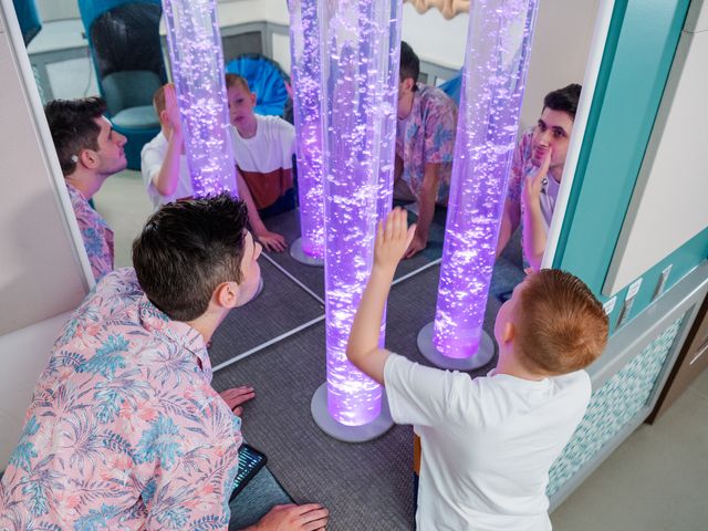 A child and an adult look at tubes filled with bubbles lit up by colored light.