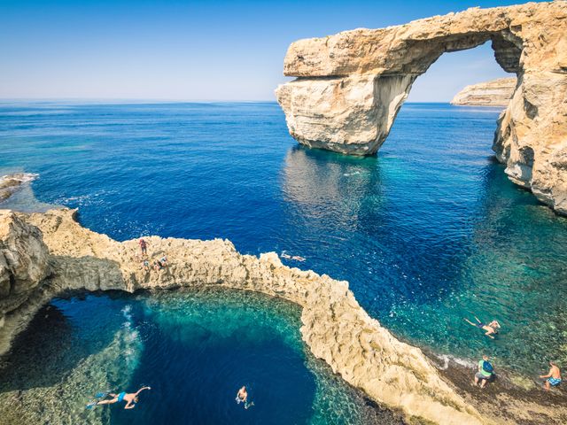 The world famous Azure Window in Gozo island Malta with arched rock formations and people swimming in the turquoise blue water.