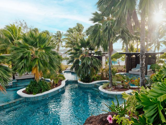 A lagoon-style pool surrounded by palm trees with sunlight shining through at The St. Regis, Bora Bora.