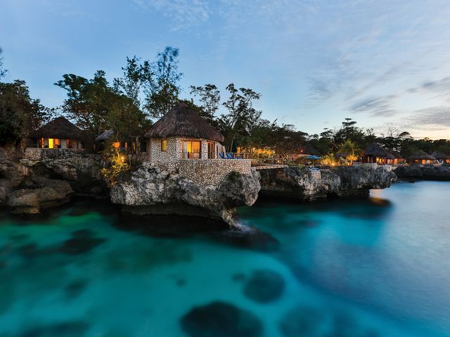 Thatched huts edging a rocky cliff alongside the ocean with turquoise water.