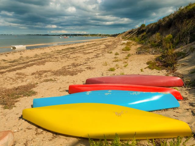 Four colorful kayaks sit on a Nantucket Beach with a grassy bluff and some sea grass.