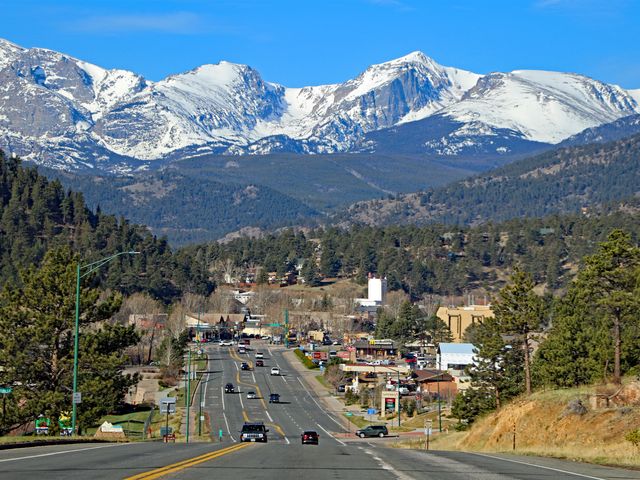A road heading down a hill leads into the town of Estes Park surrounded by mountain scenery.