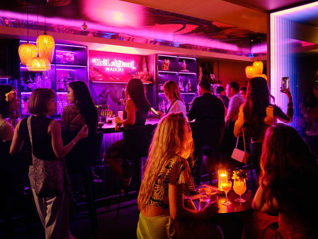 A buzzy scene with a crowded bar area and neon pink lighting at The Lei Stand at Romer House Waikiki.