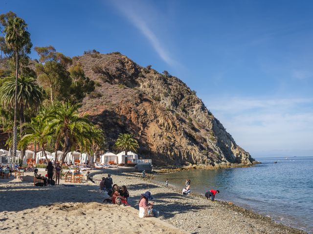 A beach club with cabanas and seating next to a rocky bluff with people sitting on the sand.