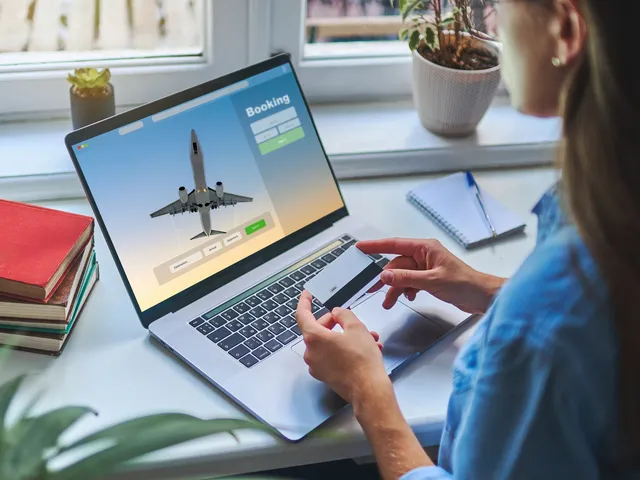 Someone is seen sitting in front of a laptop with an image of an airplane while holding a credit card.