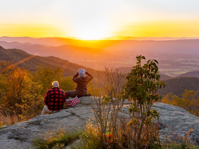 Two people sit on a rock at the top of a lookout point in Shenandoah National Park.