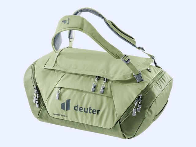 A light green duffel with carrying straps suspended in the air, against a blue background.