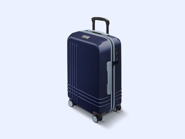 A hard carry-on plastic suitcase seen from the side, with etched criss-cross line detailing, in a navy blue color, against a blue background.