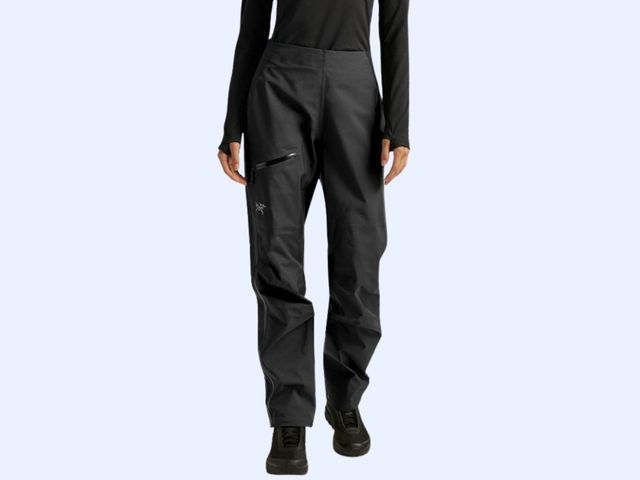 A person is seen from the waist down wearing black waterproof pants against a blue background