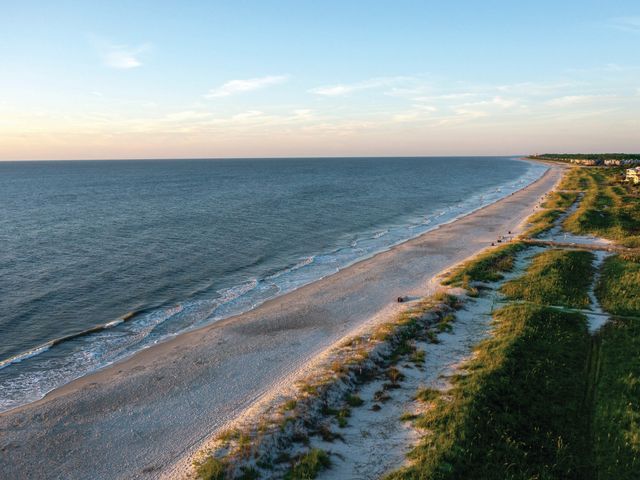 An aerial view over the sand and grassy bluffs of Hilton Head Island's coastline at sunset.