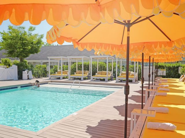 A pool area shaded by large orange umbrellas with matching sunbeds and cabanas.
