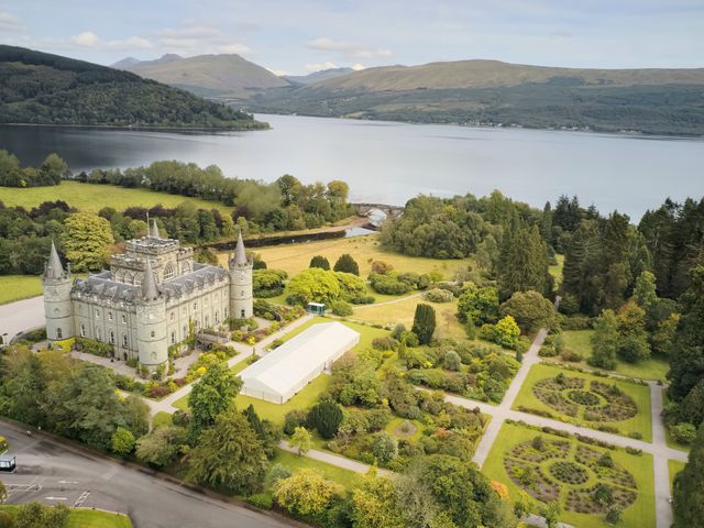 An aerial view over Inveraray Castle in Scotland with manicured gardens and trees next to a body of water.