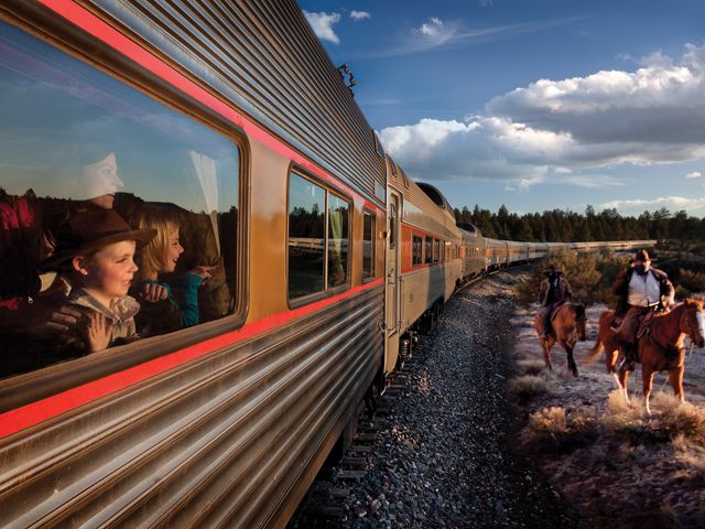 Masked horse riders next to a train car as people excitedly watch out the window.