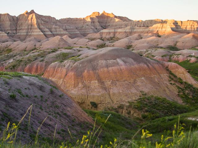 Striped rock formations at Badlands National Park topped with patches of green grass.