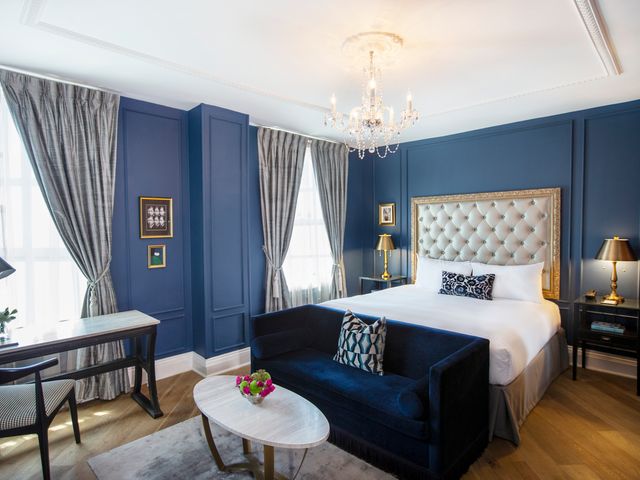 A hotel room with blue walls, grey curtains, a blue sofa, and plush bed at The Culver Hotel.
