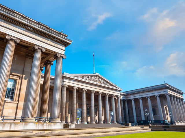The stately exterior of the British Museum with many columns and sculptures on a sunny day.