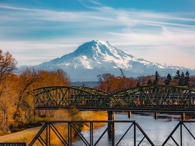 A bridge with train tracks over a river in front of Mt. Rainier.