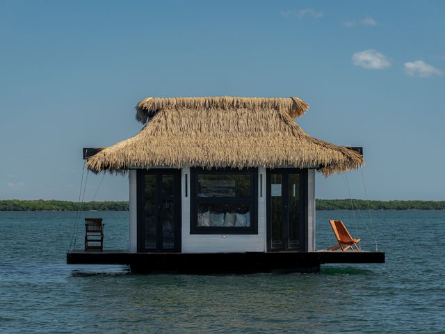 A thatched-roof bungalow floating on a body of water.