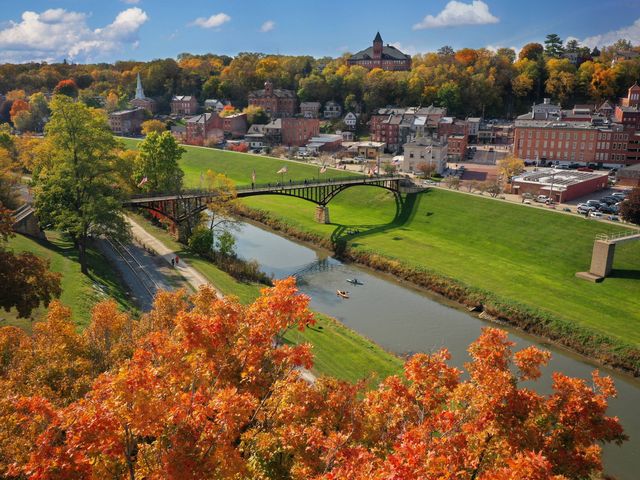 A view over the town of Galena with a river running through it and a bridge crossing, with buildings on one side and colorful fall foliage on both.