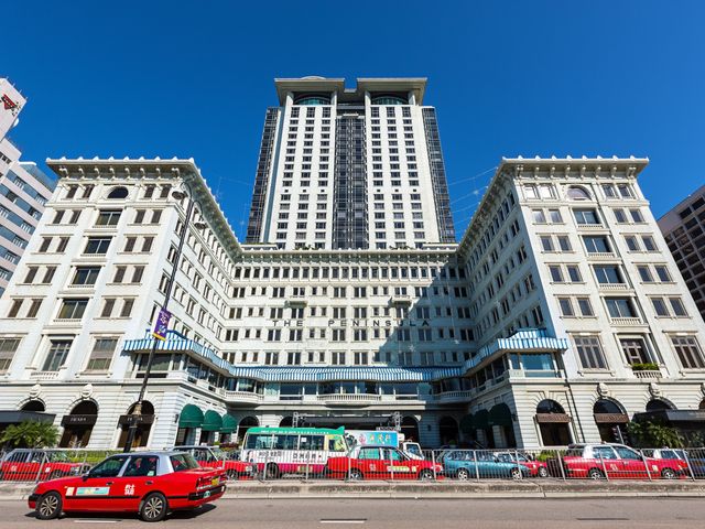 The stately exterior of the Peninsula Hong Kong with red taxis outside.