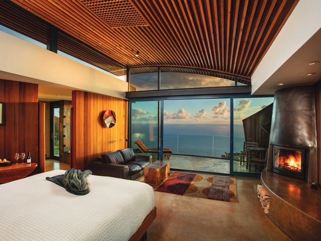 A large hotel room with a fireplace and seating area facing a balcony with unobstructed ocean views.