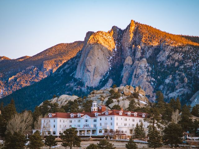 A white hotel with a red roof sitting beneath a massive mountain ridge.