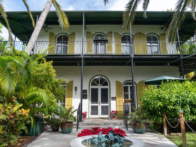The exterior of the French Colonial style home of American writer Ernest Hemingway in Key West with a porch, balcony, and windows with large shutters.