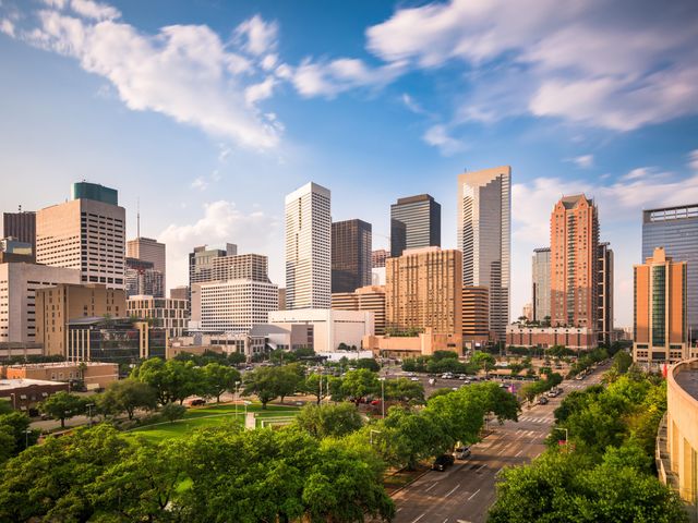 The Houston skyline next to a leafy green park under a blue sky.
