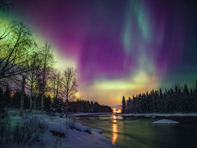 Purple, yellow, and green northern lights in Rovaniemi, Finland over a river with snow on each side.