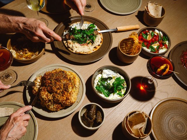 An overhead view of hands reaching into a table full of food with dim lighting.