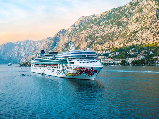 The Norwegian Gem ship is seen sailing next to a mountainside village in Europe.