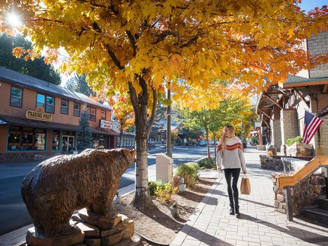 A woman walks along a tree-lined street with yellow and orange leaves and a bear statue.