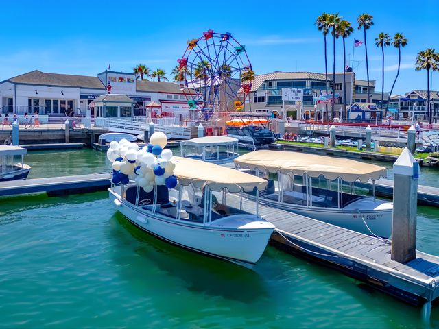 A few Duffy electric boats, one with balloons attached, at a pier in front of the Balboa Fun Zone in Newport Beach.