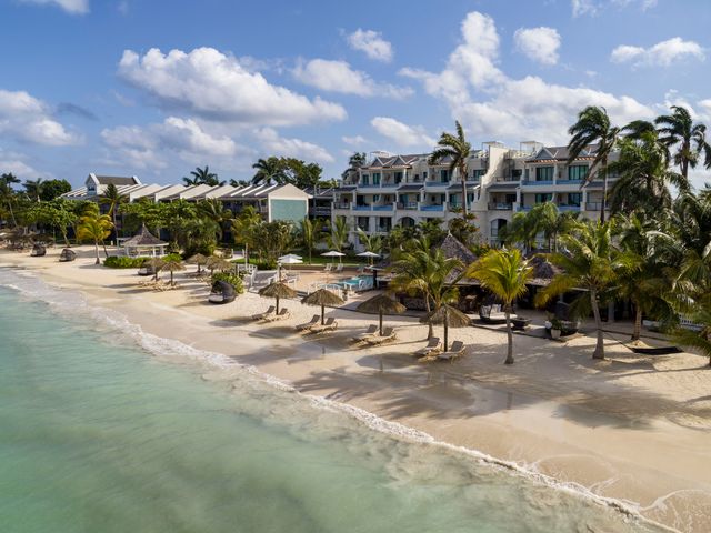 The beachfront area of Sandals Negril with thatched umbrellas shading pairs of lounge chairs and rows of palm trees facing the turquoise water.