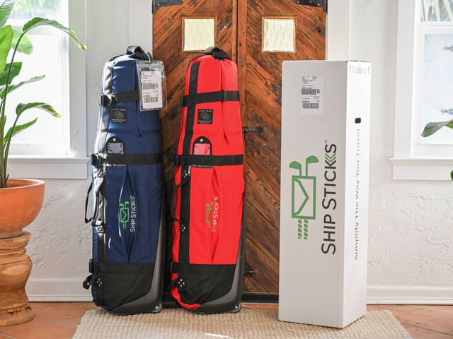 Red and blue golf bags propped up against a wood wardrobe next to a box for shipping them.